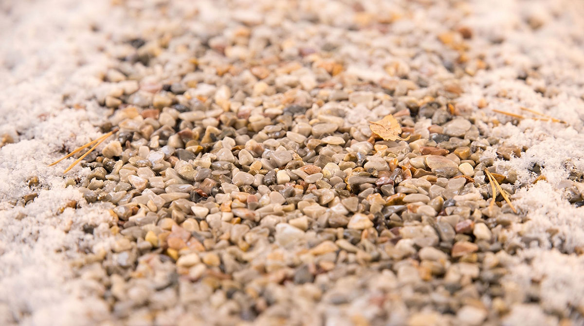 Nahaufnahme eines Steinteppichs mit kleinen Kieseln und leichtem Schneebedeckung